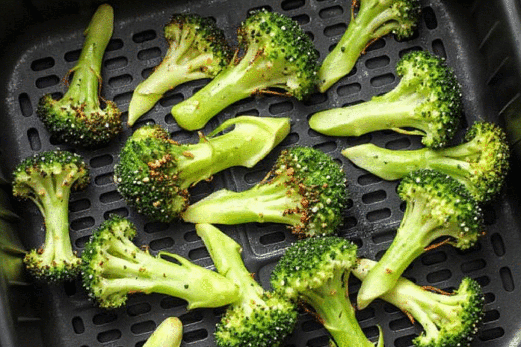 Side-by-side image showing seasoned raw broccoli and the same broccoli cooking in an air fryer.