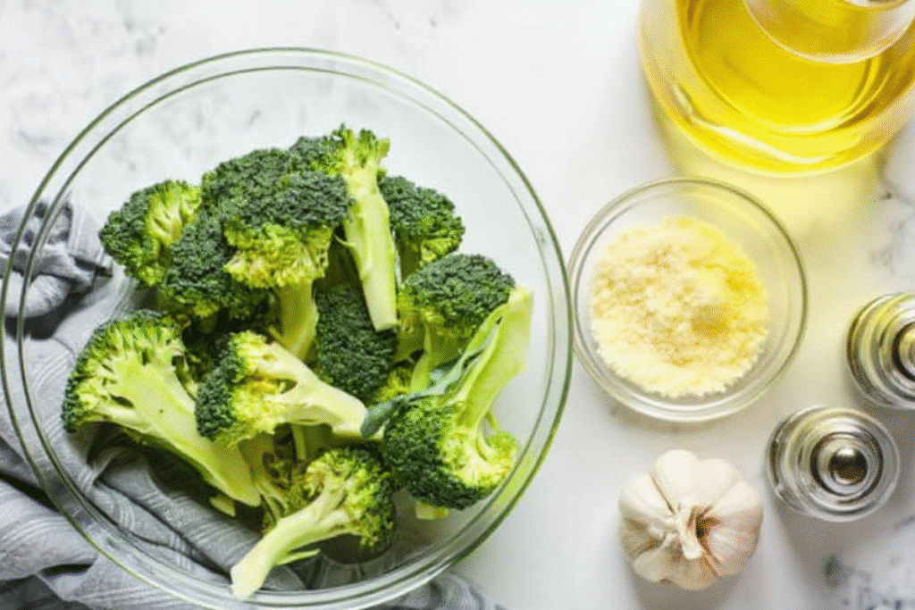 A prep station with Air Fryer Broccoli with Garlic, Parmesan cheese, garlic, olive oil, salt, and pepper.
