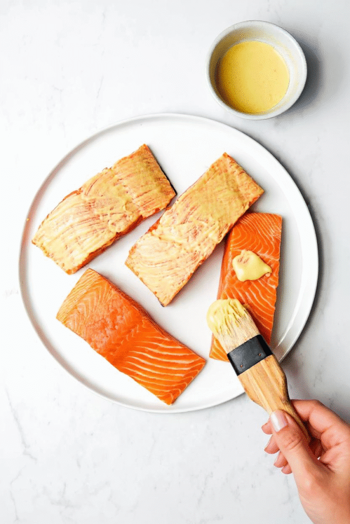 Brushing mustard marinade onto salmon fillets before air frying.