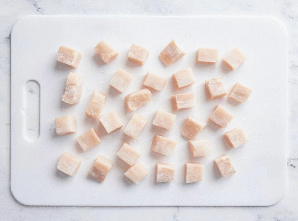 Frozen chicken cubes arranged neatly on a white cutting board.