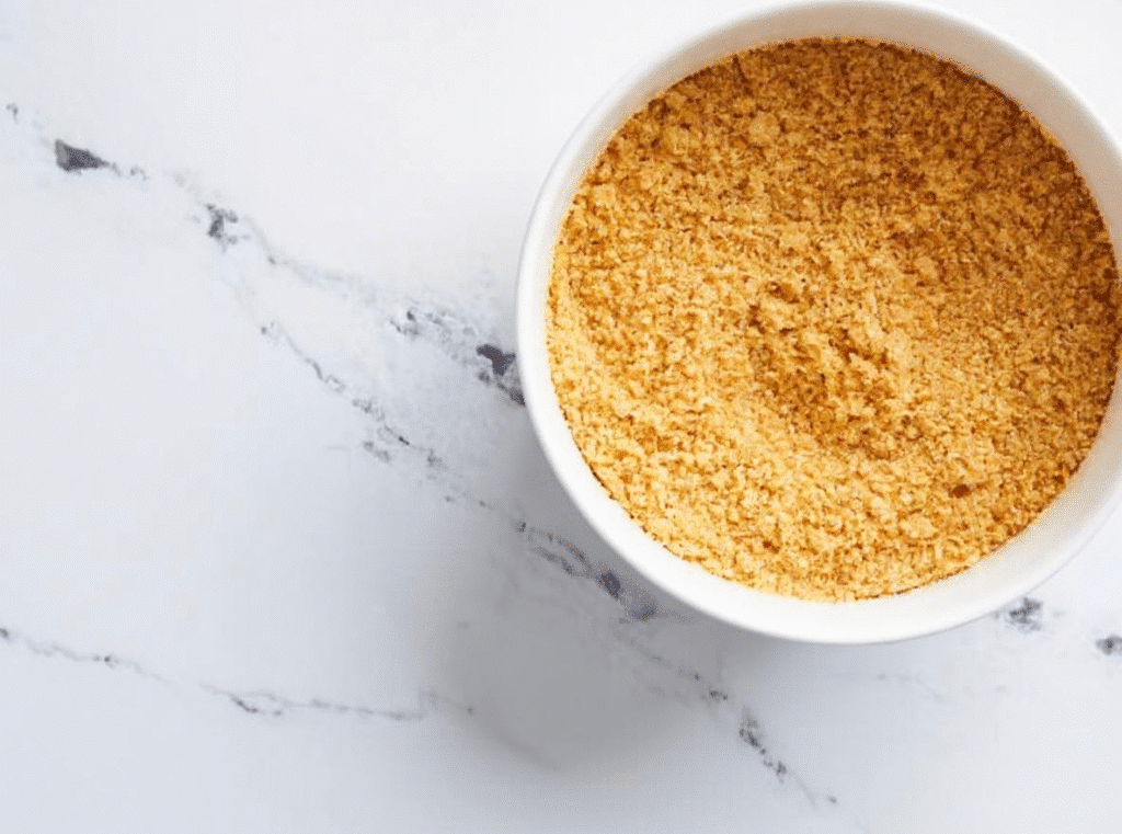White bowl filled with golden seasoned breadcrumbs on a marble surface.