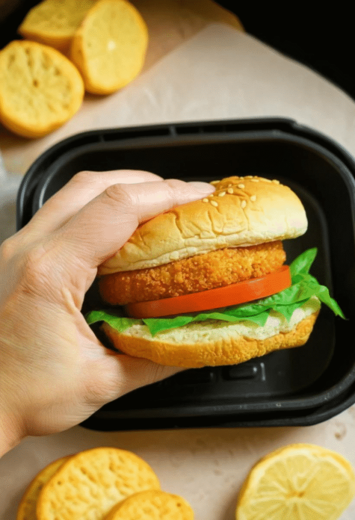 Hand holding a chicken sandwich made with air fried patty, lettuce, and tomato