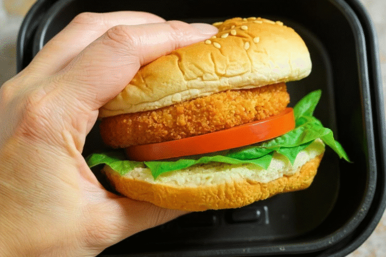 Hand holding a chicken sandwich made with air fried patty, lettuce, and tomato