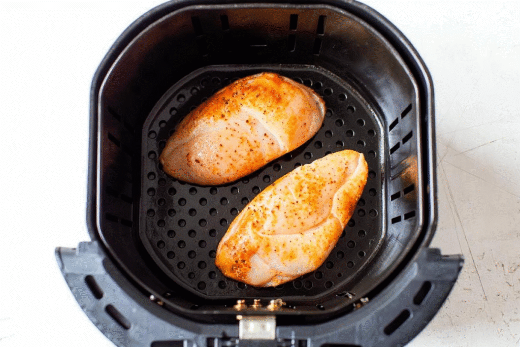 Seasoned raw chicken breasts placed inside an air fryer basket.