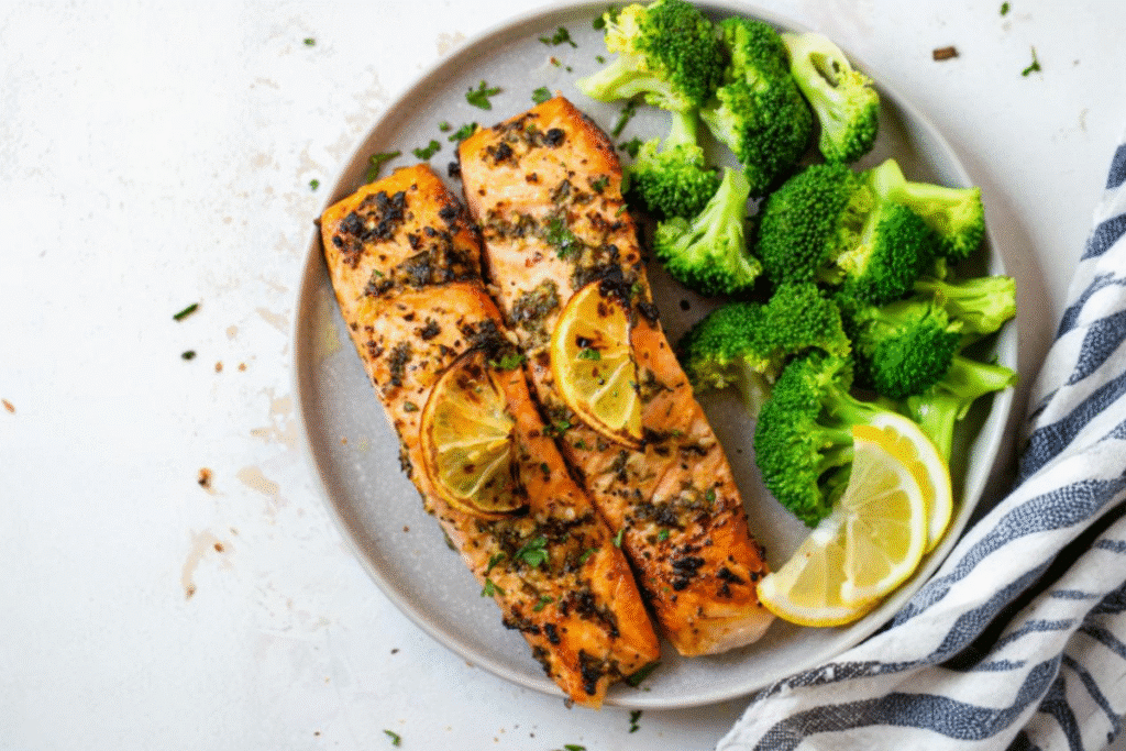 Single-Serve Air Fryer Salmon with Garlic Lemon Butter fillets served with steamed broccoli and lemon wedges on a gray plate.