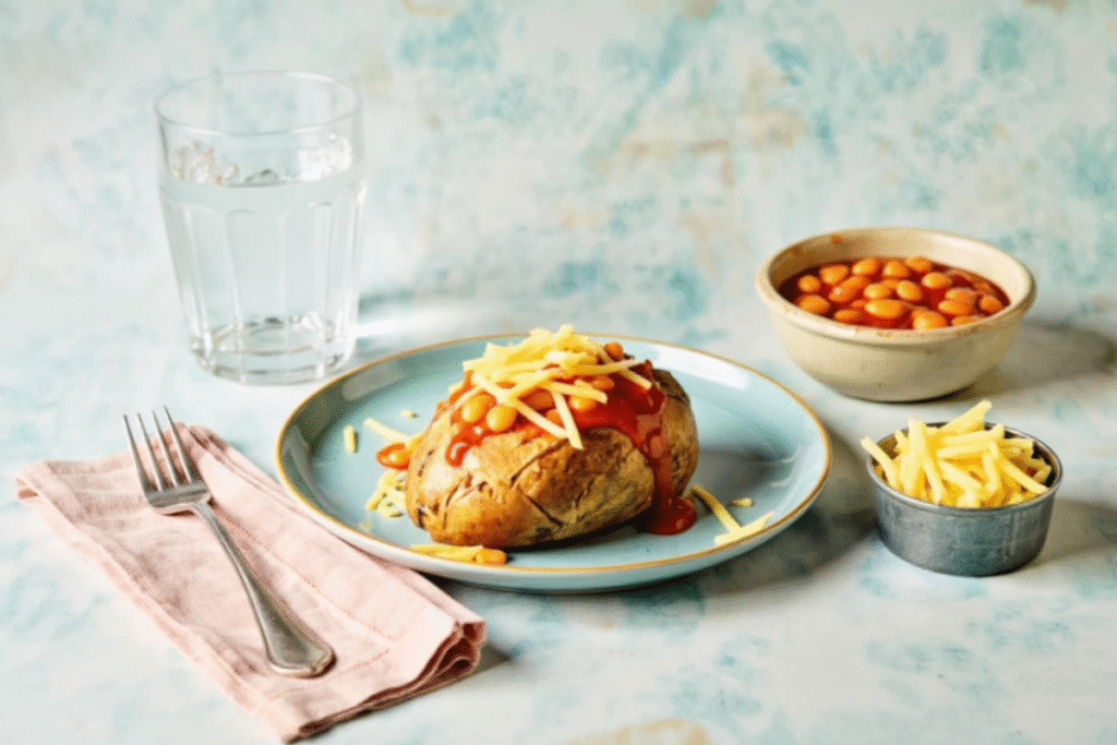 Baked potato topped with cheese and baked beans, served with extra toppings and a glass of water.