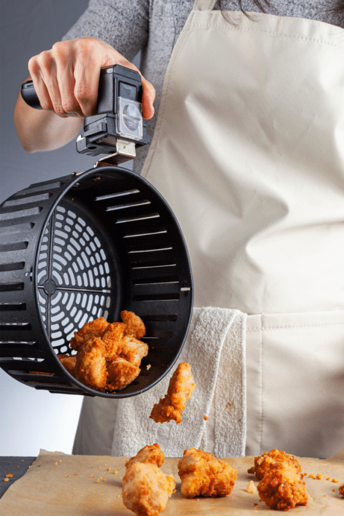 Hand dumping crispy chicken pieces from air fryer basket onto parchment paper