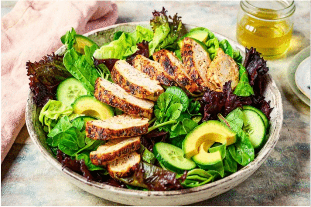 Sliced air fryer chicken breast served over a fresh green salad with avocado and cucumbers.