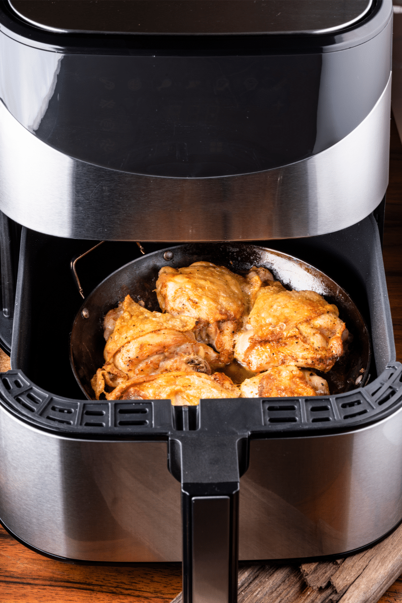 Air fryer basket with roasted chicken thighs inside , see our air fryer buying guide