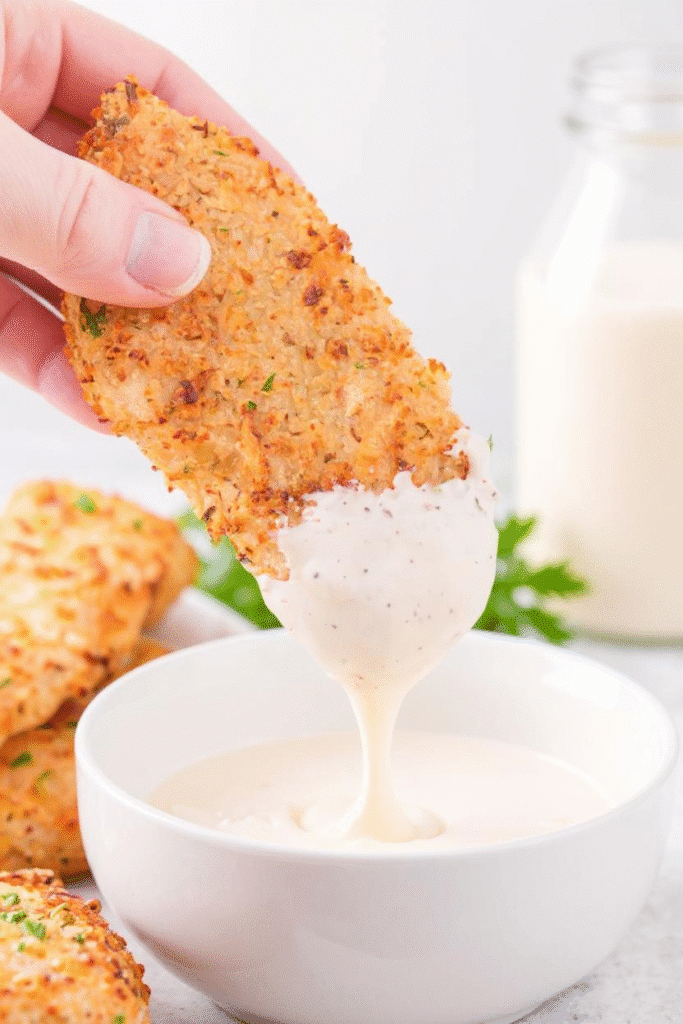 Hand dipping crispy ranch air fryer chicken tender in ranch sauce