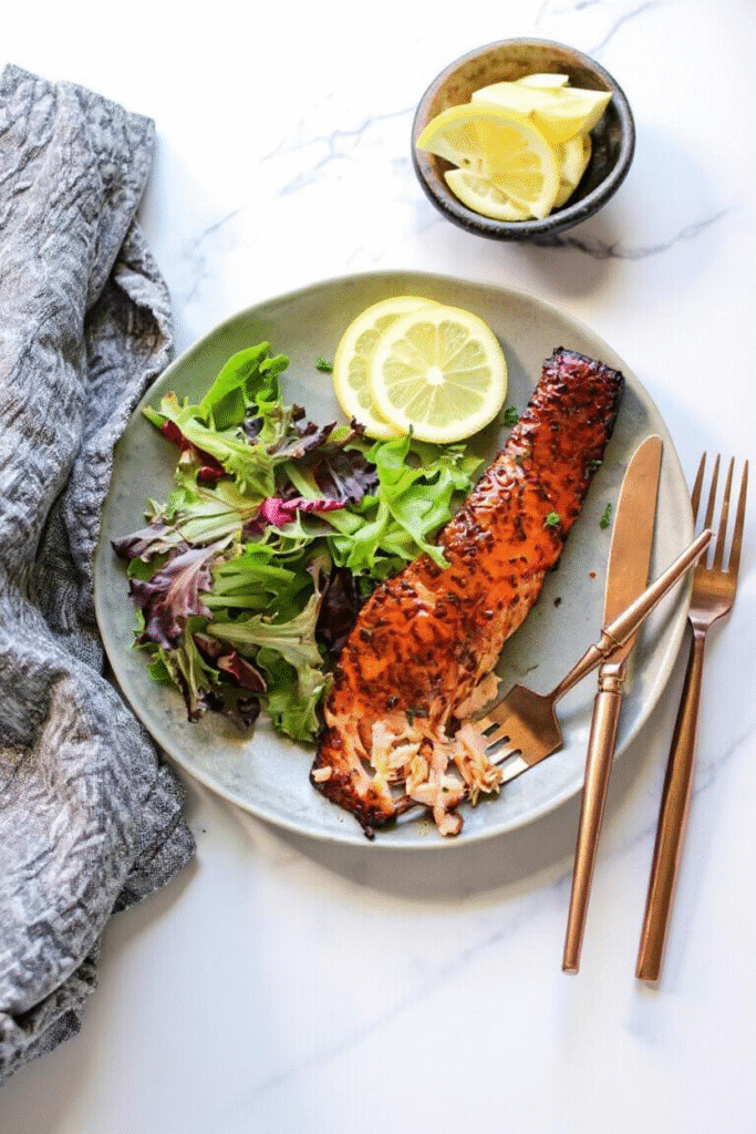Partially eaten Air Fryer Honey Mustard Salmon fillet with salad and lemon on a ceramic plate.